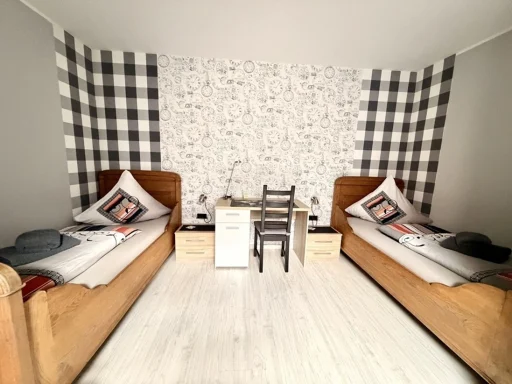 Modern eingerichtetes Zweibettzimmer in einer Pension in Legden mit zwei Holzbetten, Schreibtisch und gemusterter Tapete.