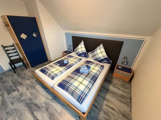 Gemütliches Doppelzimmer mit Dachschräge in einer Pension in Legden, ausgestattet mit einem Holz-Doppelbett, blau-weiß karierter Bettwäsche
